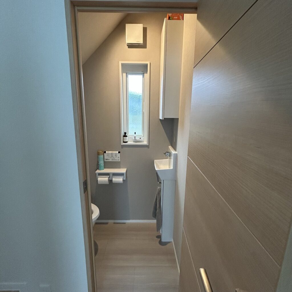 我が家の階段下トイレを入口から見たところ。左に便器、正面に小窓、右に手洗いと吊戸棚