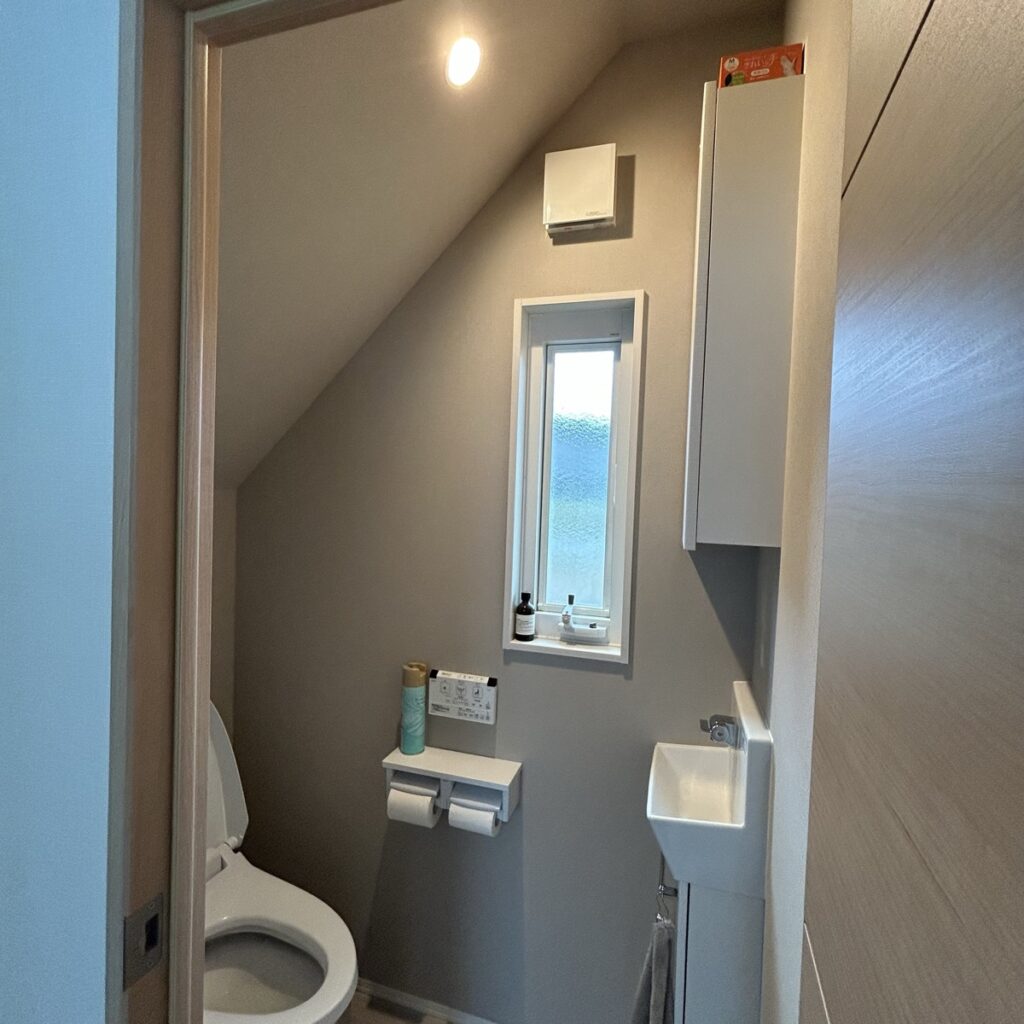 我が家の階段下トイレ。天井は手洗い側が高く、便器の後ろに向かって斜めに下がっている